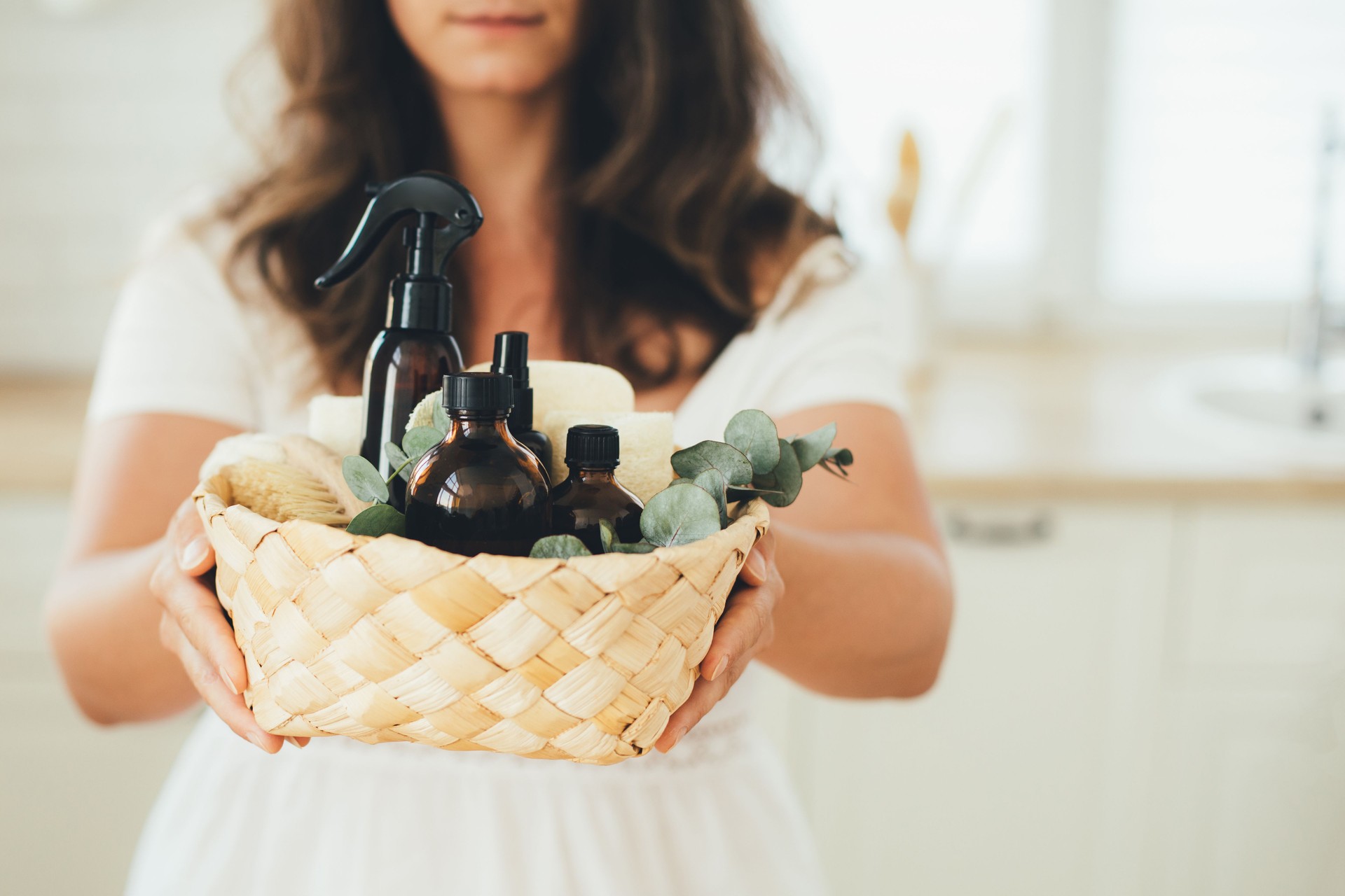 Woman holding wicker basket with natural eco-friendly zero waste plastic free cleaning items: brushes, rugs, soap, essential oils, spray and sponges at the kitchen.